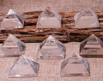 May include: Nine clear quartz crystal pyramids arranged in a row on a brown burlap background. The pyramids are all the same size and shape, and they are all facing the camera.