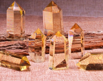May include: A collection of seven clear quartz crystal points with a golden yellow hue. The crystals are arranged on a brown burlap surface with a piece of weathered wood behind them.