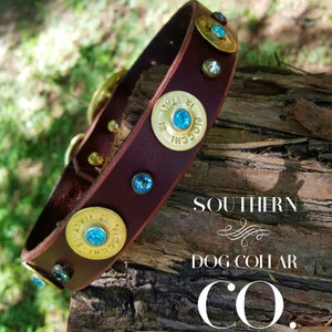 Op de afbeelding: Een bruine leren hondenriem met gouden schotpatronen accenten en blauwe strass steentjes. De riem ligt op een houten oppervlak met de tekst "SOUTHERN DOG COLLAR CO." eronder gedrukt.