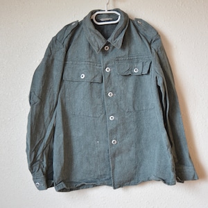 May include: A long-sleeved, dark green work shirt with a button-up front and two flap pockets. The shirt has a collar and is made of a textured fabric.
