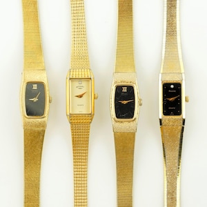May include: Four gold-coloured wristwatches with rectangular and oval faces. The watch faces are black, cream, and gold, with gold hands and Roman numeral hour markers. The watch bands are gold, with a mesh or textured design.