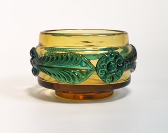 May include: A small amber glass bowl with a green and blue leaf design around the rim.