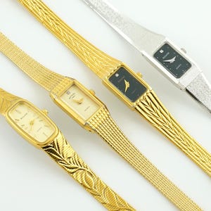 Könnte beinhalten: Vier Vintage-Armbanduhren mit Gold- und Silberbändern. Die Uhren haben rechteckige und ovale Zifferblätter mit goldenen und schwarzen Zifferblättern. Eine Uhr hat einen Diamantakzent. Die Bänder haben strukturierte und gemusterte Designs.