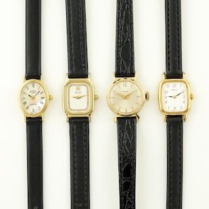 Puede incluir: Se muestran cuatro relojes de pulsera dorados vintage con correas de cuero negro. Cada reloj tiene un diseño de esfera diferente, incluyendo números romanos y un segundero. Los relojes están dispuestos verticalmente sobre un fondo blanco.