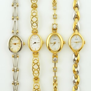 Könnte beinhalten: Vier gold- und silberfarbene Damenuhren mit ovalen Zifferblättern und verschiedenen Banddesigns. Die Zifferblätter sind weiß oder cremefarben, mit schwarzen Zeigern und Stundenmarkierungen. Eine Uhr hat ein silbernes Armband, die anderen sind goldfarben.