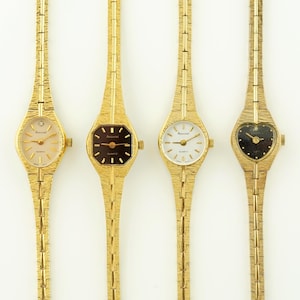 Op de afbeelding: Vier goudkleurige Accurist quartz horloges met getextureerde bandjes. De wijzerplaten zijn ovaal, vierkant, rond en hartvormig, met champagne, zwart en wit. Elk horloge heeft een delicate, getextureerde band.