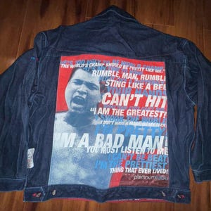 Puede incluir: Chaqueta vaquera azul oscuro con un gran gráfico en la espalda. El gráfico presenta un retrato y el texto "I'M A BAD MAN". La chaqueta tiene cierre de botones y detalles rojos.