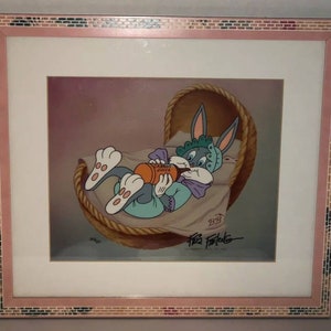 Puede incluir: Arte de dibujos animados enmarcado con el personaje de Bugs Bunny bebé en una cuna de mimbre, bebiendo jugo de zanahoria. La obra está firmada por Friz Freleng y tiene un marco rosa y con diseño de mosaico.