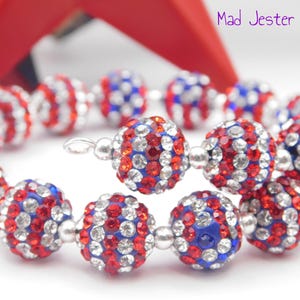May include: A spiral bracelet featuring spherical beads encrusted with red, white, and blue rhinestones, separated by small silver-toned metal spacers. The text Mad Jester Jewelry is visible in the upper right corner of the image.