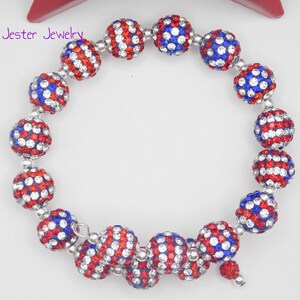 May include: A wrap bracelet featuring spherical beads covered in red, white, and blue crystals. The beads are arranged in a circular pattern with silver-toned spacers. The text Mad Jester Jewelry is visible in the upper left corner of the image.