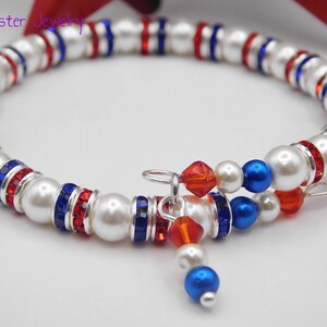May include: A wrap bracelet featuring white faux pearls, red and blue crystal rondelles, and silver-tone spacers. The design includes dangling charms with red and blue beads. The text Mad Jester Jewelry is visible in the upper left corner.