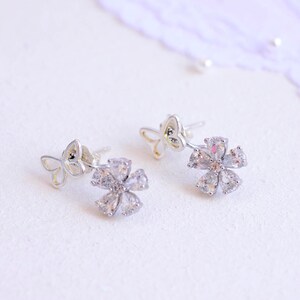 May include: A pair of silver earrings with a flower design. Each earring features a small butterfly charm and a larger flower charm with clear cubic zirconia stones.