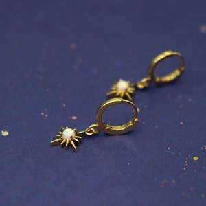May include: A pair of gold hoop earrings with a dangling star charm featuring a white opal stone.