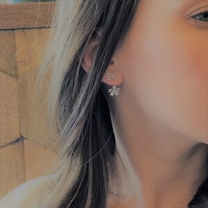 May include: A pair of silver earrings featuring a butterfly design on one ear and a flower design with clear stones on the other ear.