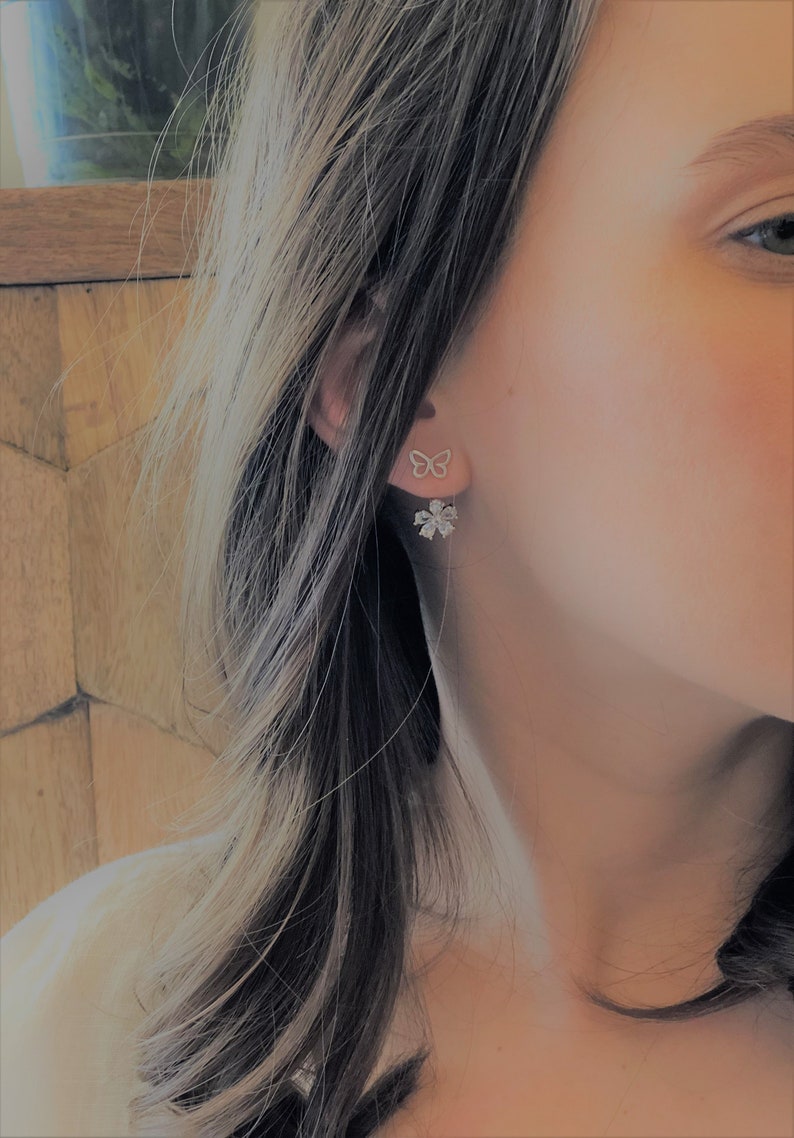 May include: A pair of silver earrings featuring a butterfly design on one ear and a flower design with clear stones on the other ear.