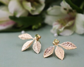 May include: A pair of gold leaf earrings with green gemstones. The earrings are delicate and feature a three-leaf design.