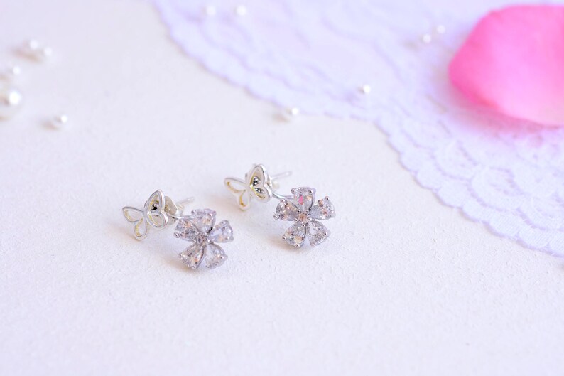 May include: A pair of silver earrings with a flower design. Each earring features a small butterfly charm and a larger flower charm with clear cubic zirconia stones.