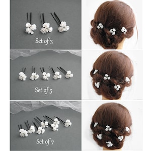 May include: Three sets of white flower hair pins. The first set has three pins, the second set has five pins, and the third set has seven pins. Each pin has a small cluster of white flowers.