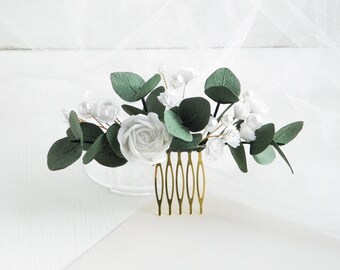 May include: A gold hair comb with white flowers and green leaves. The comb is decorated with small white pearls.