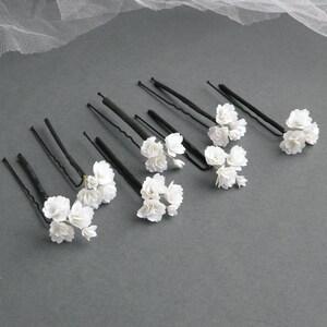 May include: Set of eight black hair pins with white flower accents. Each pin has a small cluster of white flowers.