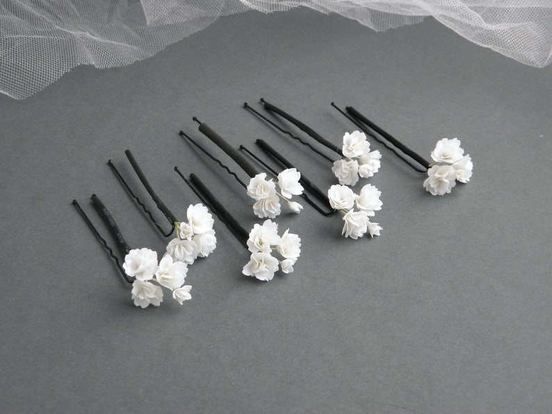 May include: Set of eight black hair pins with white flower accents. Each pin has a small cluster of white flowers.