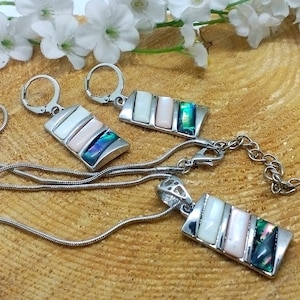 May include: A silver necklace and earrings set with a pendant and earrings featuring a rectangular design with three layered iridescent shell pieces in shades of white, pink, green, and blue.