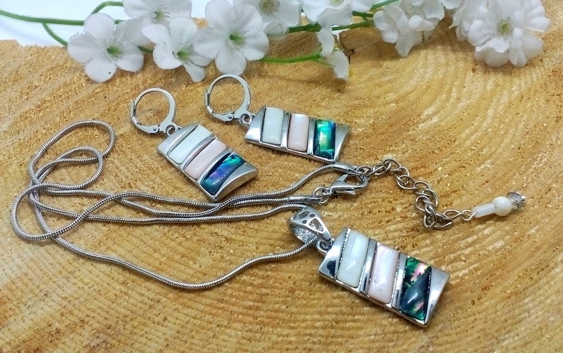 May include: A silver necklace and earrings set with a pendant and earrings featuring a rectangular design with three layered iridescent shell pieces in shades of white, pink, green, and blue.
