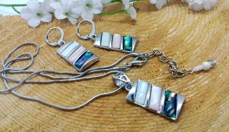 May include: A silver chain necklace with a pendant and matching earrings. The pendant and earrings feature a rectangular design with multiple iridescent shell pieces in shades of white, pink, and green.
