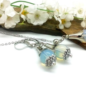 Puede incluir: Un collar de cadena de plata con un colgante de &oacute;palo en forma de l&aacute;grima y pendientes a juego. El colgante y los pendientes tienen un dise&ntilde;o floral plateado.