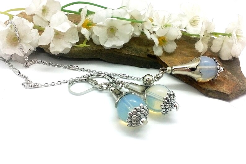Puede incluir: Un collar de cadena de plata con un colgante de &oacute;palo en forma de l&aacute;grima y pendientes a juego. El colgante y los pendientes tienen un dise&ntilde;o floral plateado.