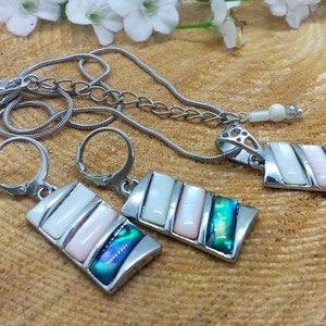 May include: A silver necklace and earrings set with a rectangular pendant and matching earrings. The pendant and earrings feature a multi-colored abalone shell inlay with white and pink accents.