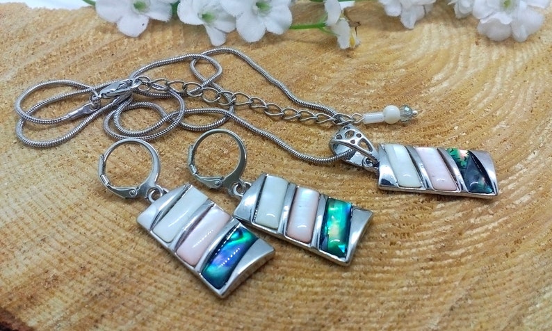 May include: A silver necklace and earrings set with a rectangular pendant and matching earrings. The pendant and earrings feature a multi-colored abalone shell inlay with white and pink accents.