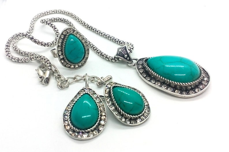 May include: A turquoise and silver necklace, earrings, and ring set. The jewellery features teardrop-shaped turquoise stones surrounded by clear rhinestones.