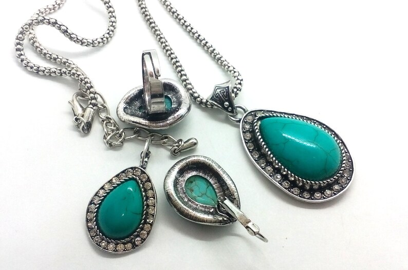 May include: A turquoise stone jewellery set with a necklace, earrings, and a ring. The stones are set in silver-toned metal with clear rhinestones.