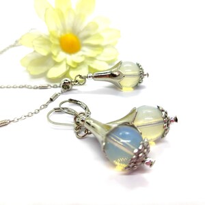 Puede incluir: Un par de pendientes de plata con una piedra de &oacute;palo en forma de l&aacute;grima y un dise&ntilde;o de flor de plata. Los pendientes cuelgan de ganchos de plata.