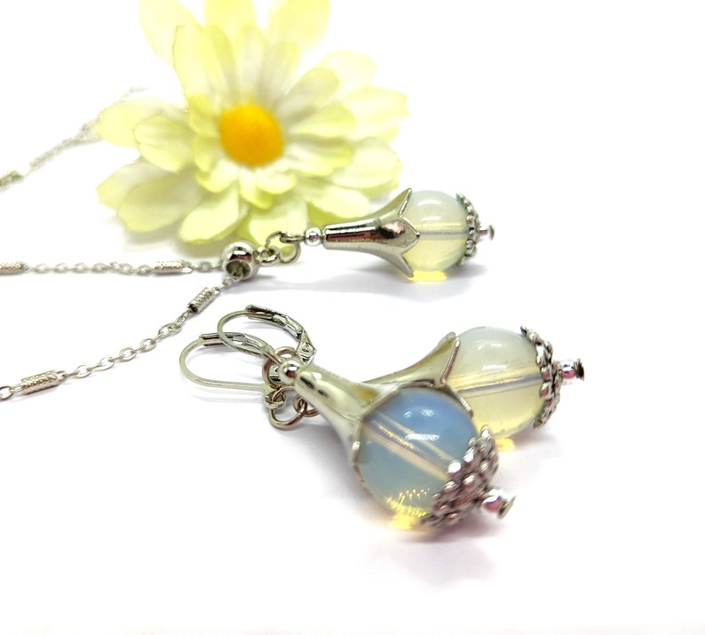 Puede incluir: Un par de pendientes de plata con una piedra de &oacute;palo en forma de l&aacute;grima y un dise&ntilde;o de flor de plata. Los pendientes cuelgan de ganchos de plata.