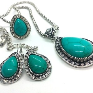 May include: A turquoise gemstone necklace and earrings set with silver chain and accents. The stones are set in a teardrop shape and surrounded by clear rhinestones.