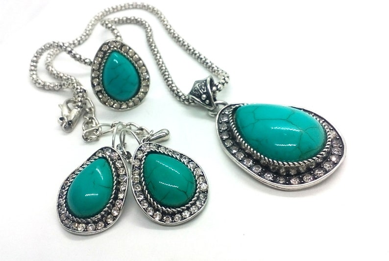 May include: A turquoise gemstone necklace and earrings set with silver chain and accents. The stones are set in a teardrop shape and surrounded by clear rhinestones.