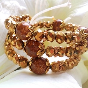 Puede incluir: Una pulsera de varias vueltas con cuentas redondas de piedra de sol marrón brillante intercaladas con cuentas metálicas doradas facetadas. Cada cuenta marrón grande está acentuada por pequeñas tapas de metal dorado en forma de hoja.