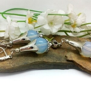 Puede incluir: Un conjunto de pendientes de plata y un colgante con una perla de &oacute;palo azul claro con un dise&ntilde;o de flor de plata. Los pendientes tienen un cierre de gancho.