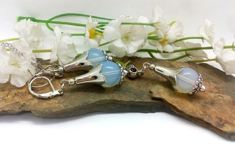 Puede incluir: Un conjunto de pendientes de plata y un colgante con una perla de &oacute;palo azul claro con un dise&ntilde;o de flor de plata. Los pendientes tienen un cierre de gancho.