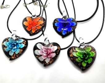Puede incluir: Cinco colgantes de cristal en forma de corazón sobre cordones negros. Cada colgante presenta una base oscura con motas doradas y una flor tridimensional tipo suculenta en naranja, azul, azul claro, rosa o verde, con una anilla de cristal.
