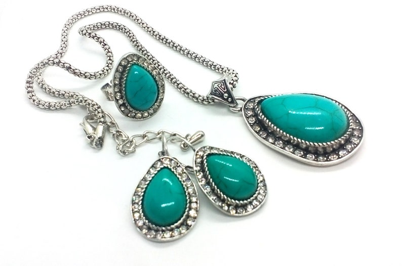 May include: A turquoise stone necklace, ring, and earrings set with silver accents. The stones are set in a teardrop shape and surrounded by clear rhinestones.