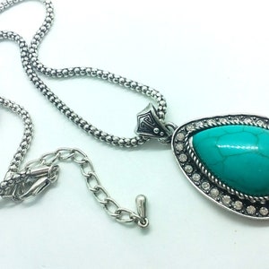 May include: A silver chain necklace with a turquoise pendant. The pendant is a teardrop shape with a silver setting and clear rhinestones.