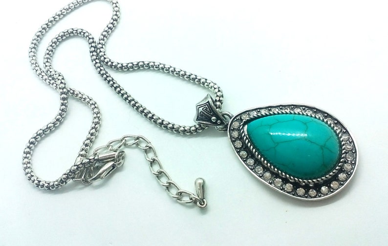 May include: A silver chain necklace with a turquoise pendant. The pendant is a teardrop shape with a silver setting and clear rhinestones.