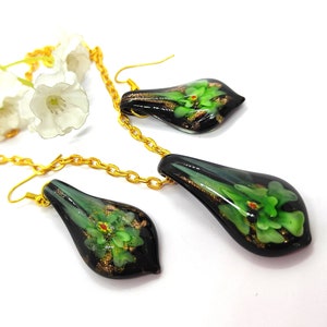 May include: A gold chain necklace and matching earrings set. The teardrop-shaped pendants are black with green floral designs and gold accents. The earrings have gold hooks. The jewelry is displayed on a white surface.