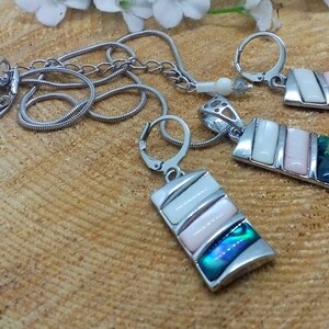 May include: A silver chain necklace with a rectangular pendant featuring white and pink abalone shell inlay. Matching earrings with the same design are also included.