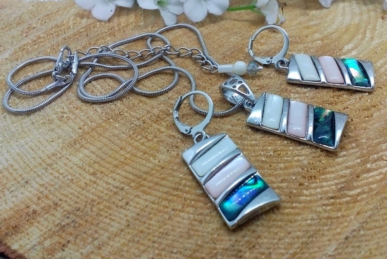 May include: A silver chain necklace with a rectangular pendant featuring white and pink abalone shell inlay. Matching earrings with the same design are also included.