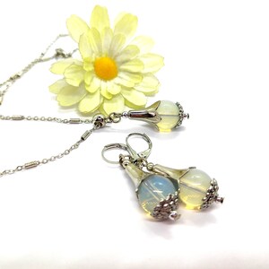 Puede incluir: Un collar de cadena de plata con un colgante de &oacute;palo en forma de l&aacute;grima y pendientes a juego. El colgante y los pendientes tienen un dise&ntilde;o floral plateado.