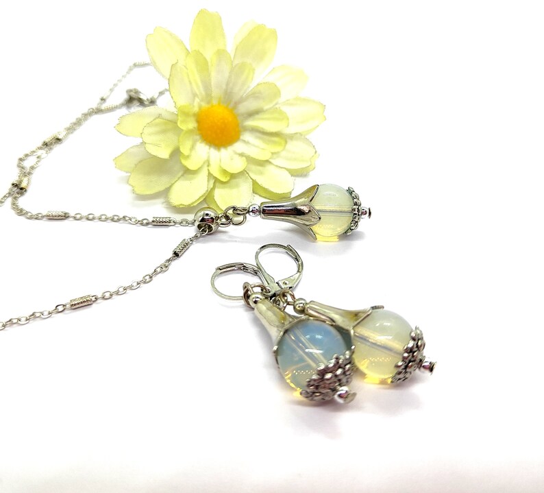 Puede incluir: Un collar de cadena de plata con un colgante de &oacute;palo en forma de l&aacute;grima y pendientes a juego. El colgante y los pendientes tienen un dise&ntilde;o floral plateado.